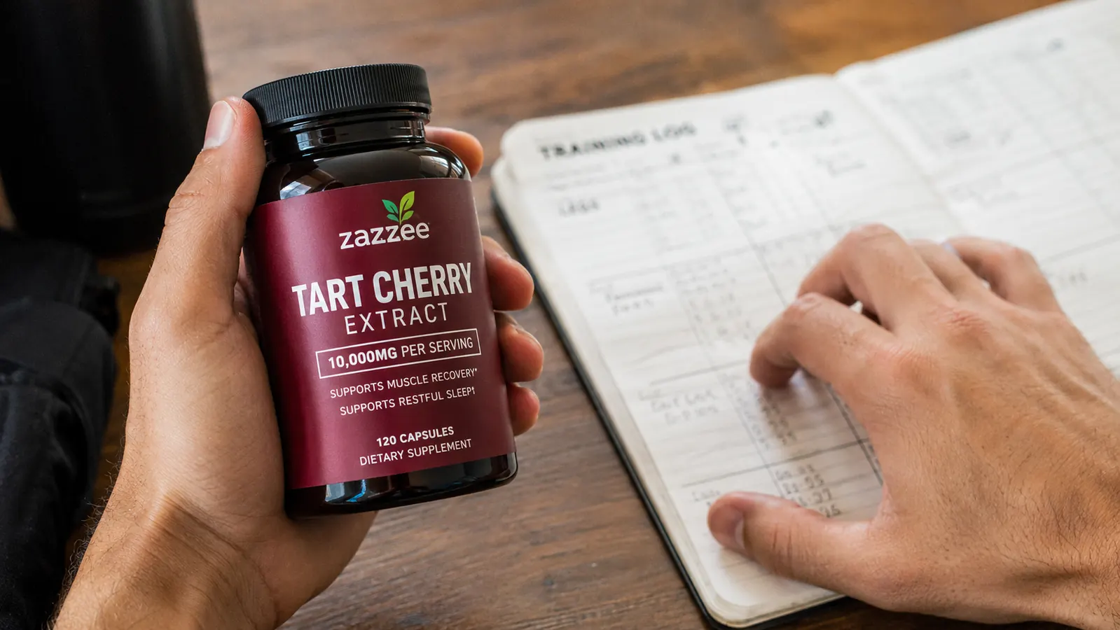 Hand holding a tart cherry extract capsule bottle with training notebook in background