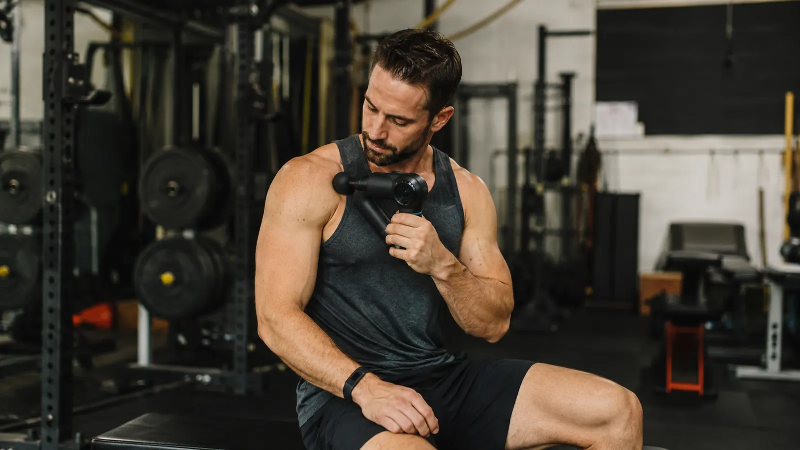 Man using a percussion massage gun on his upper trapezius after a workout
