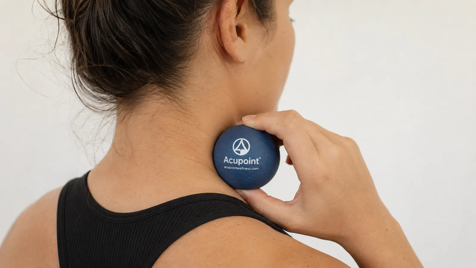Close-up of a hand pressing a massage therapy ball against the upper trapezius muscle near the neck