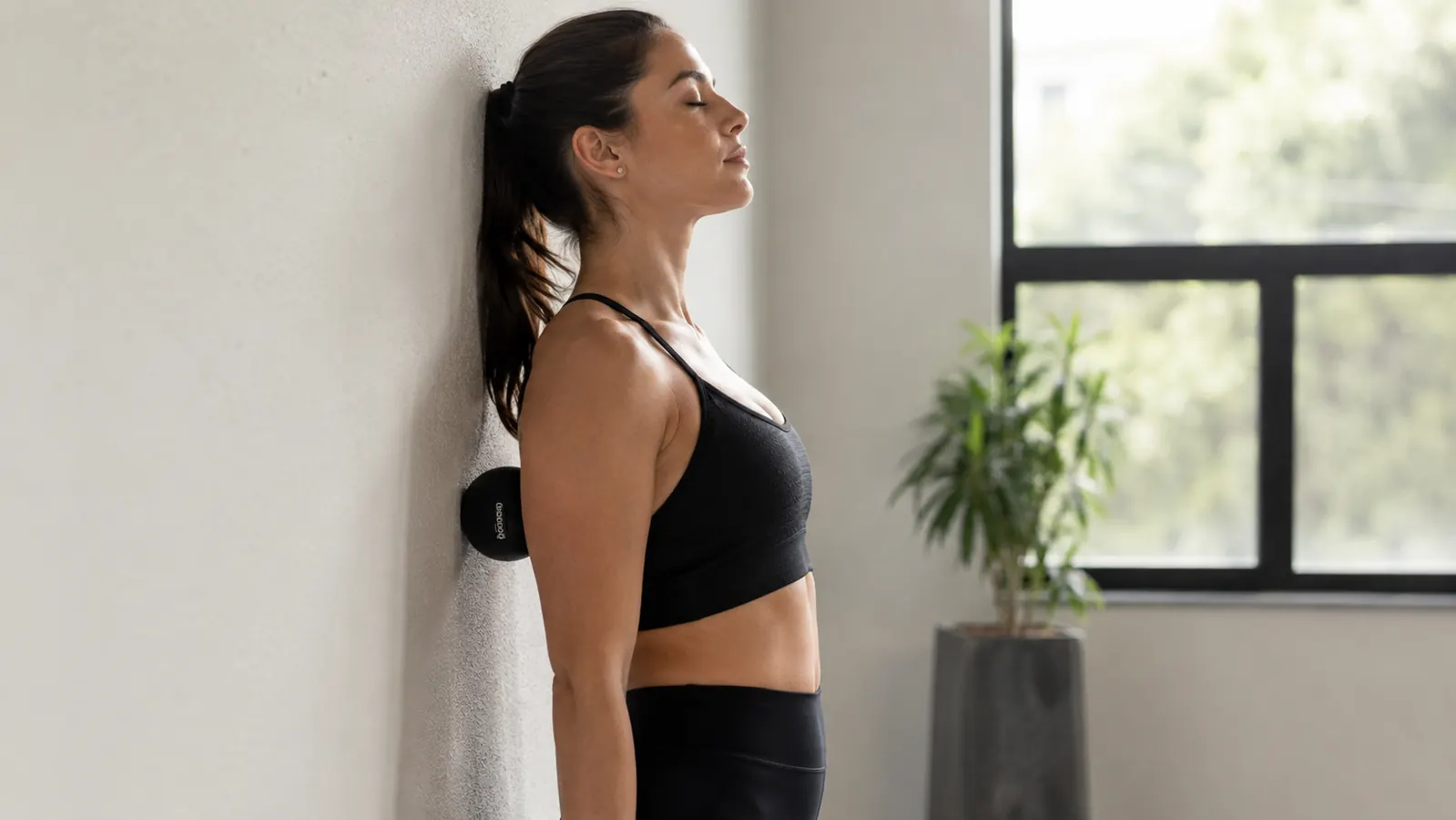 Person leaning against a wall with a massage ball positioned between their upper back and the wall