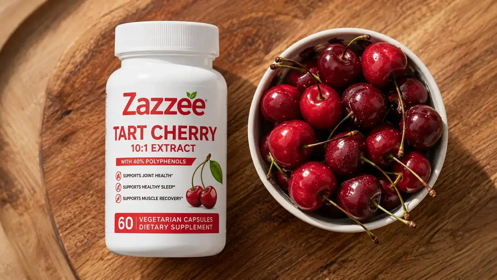 Zazzee tart cherry bottle beside a small ceramic bowl of fresh tart cherries on a wood surface