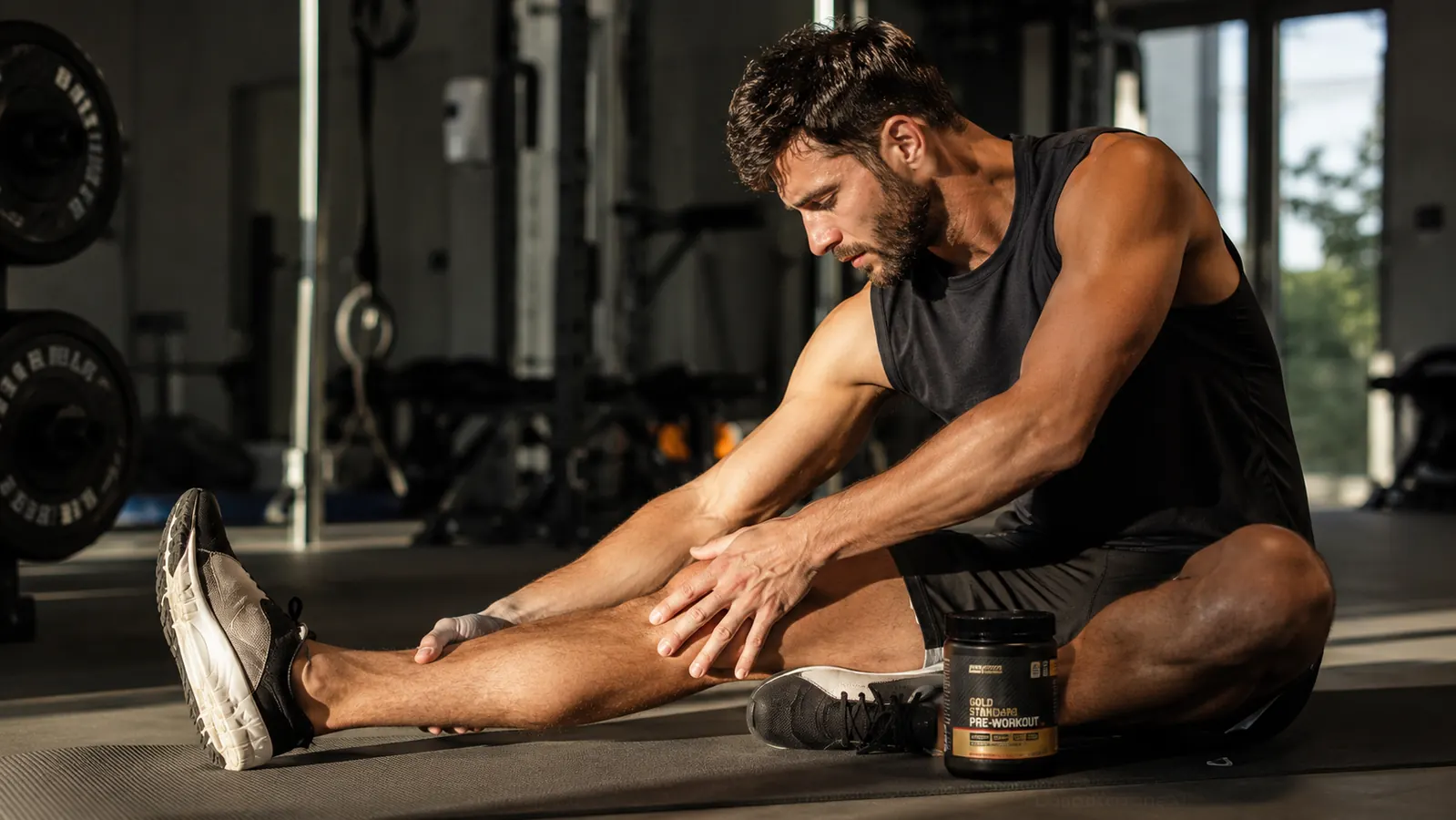 Athlete sitting on a mat stretching calves after a workout, recovery supplements on the floor nearby